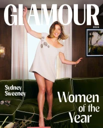 Sydney Sweeney standing on a green velvet sofa wearing a short cream dress for Glamour Magazine