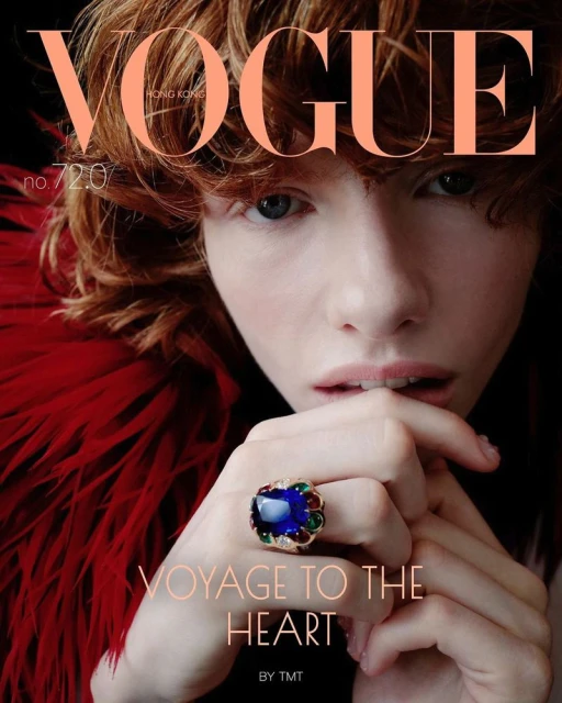 Vogue Hong Kong cover featuring a close-up of a red-haired young woman with a large blue gemstone ring, red feathered garment, and dark background.