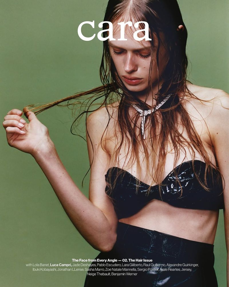 Close-up of a young adult woman with wet hair, wearing a black strapless top and a statement necklace, against a solid green backdrop.