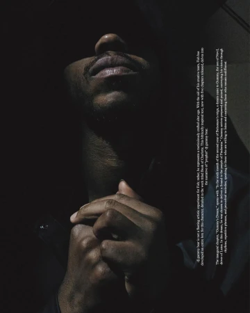 Close-up of Black adult male in a low key portrait. The man is looking up with hands clasped in an indoor environment.