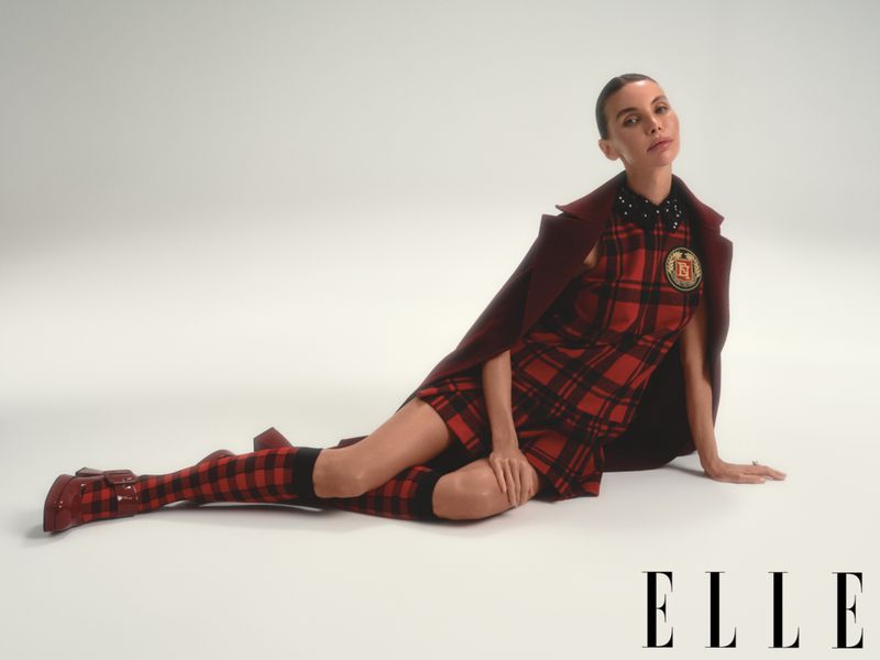 A woman in a red plaid dress and matching socks poses while reclining against a light background in a studio fashion shot.