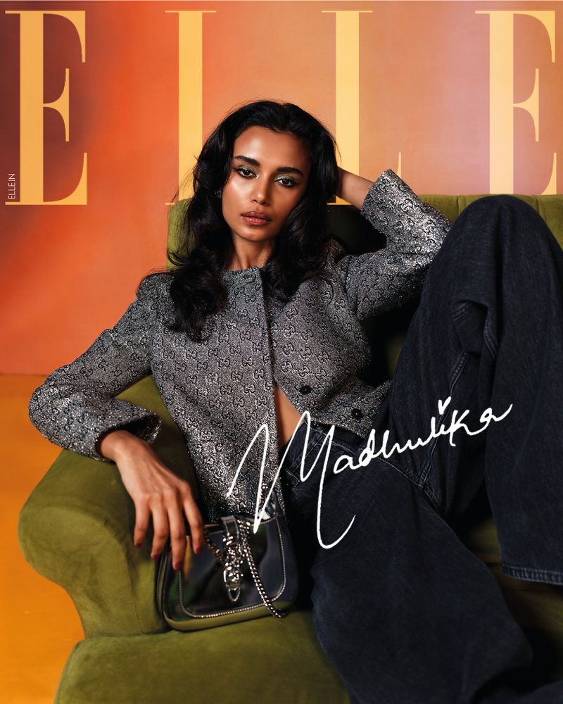 Fashion editorial shot of a South Asian woman on a green velvet couch wearing a silver jacket, black pants, and a silver purse.