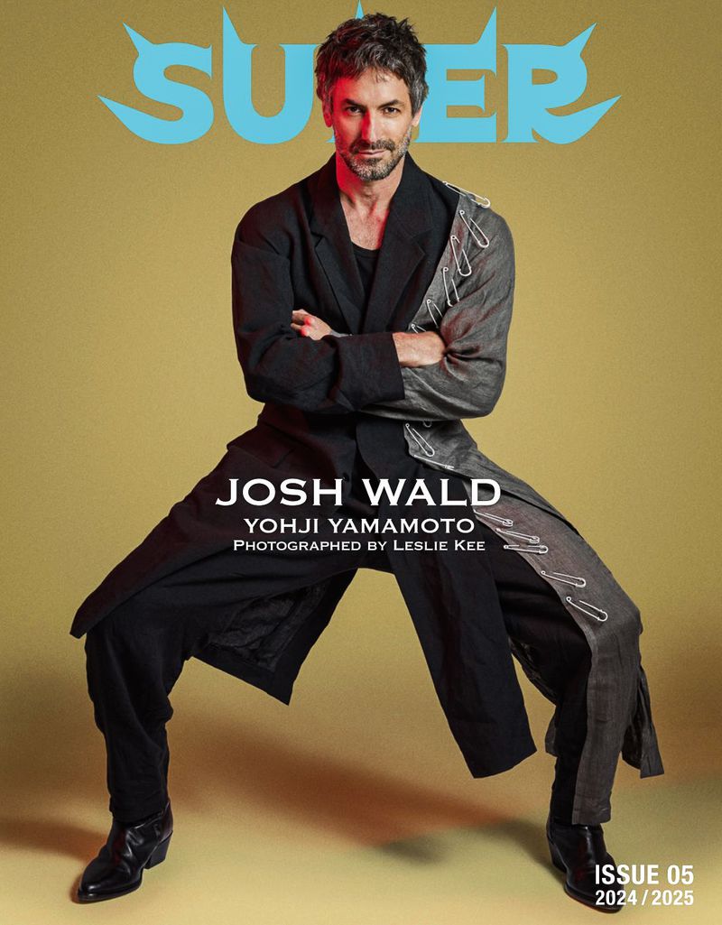 Magazine cover featuring an adult man in a coat and pants, in a wide stance against a muted yellow background.