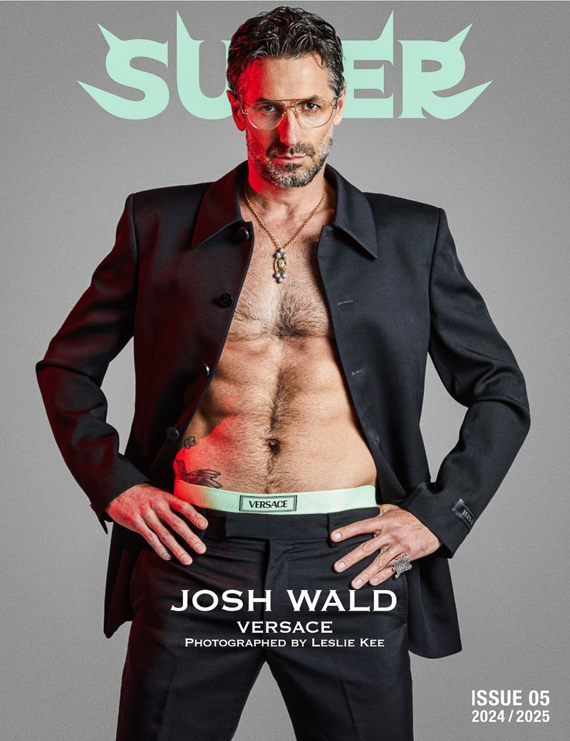 Magazine cover shot of a male model with an open jacket revealing his torso and wearing a Versace waistband, posing in a studio.