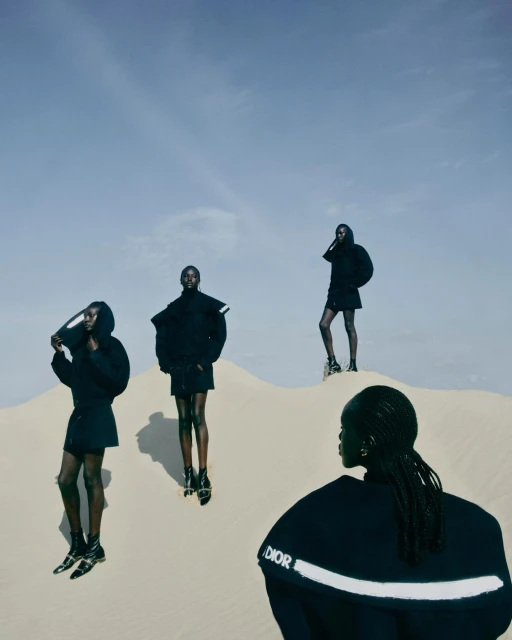 Fashion editorial featuring four Black female fashion models posing in black outfits against a desert backdrop with a clear blue sky.