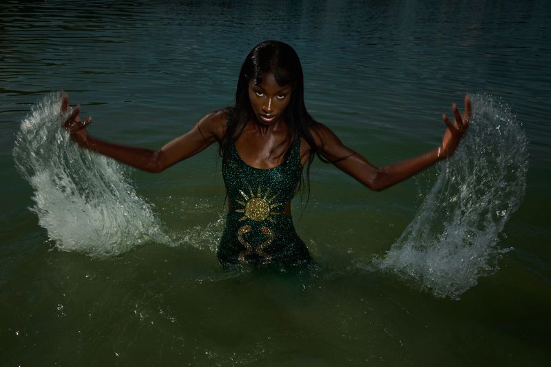 A striking photo of an adult woman with dark skin wearing a dress in a body of water, captured with a wide shot and natural light.