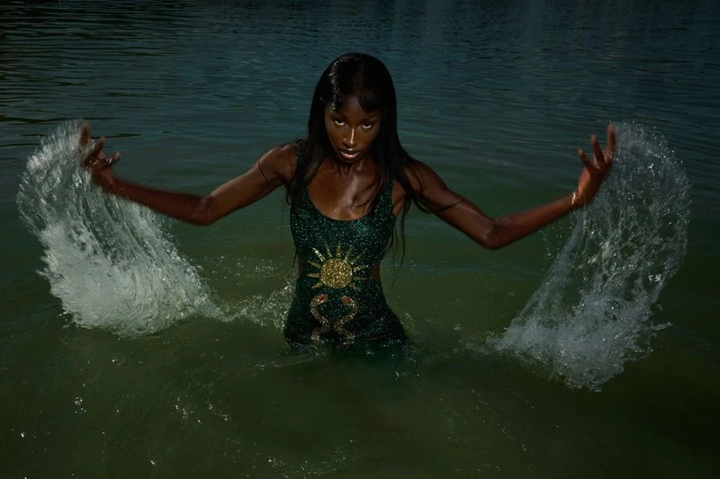 A striking photo of an adult woman with dark skin wearing a dress in a body of water, captured with a wide shot and natural light.
