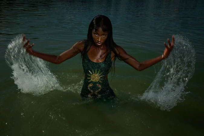 A striking photo of an adult woman with dark skin wearing a dress in a body of water, captured with a wide shot and natural light.
