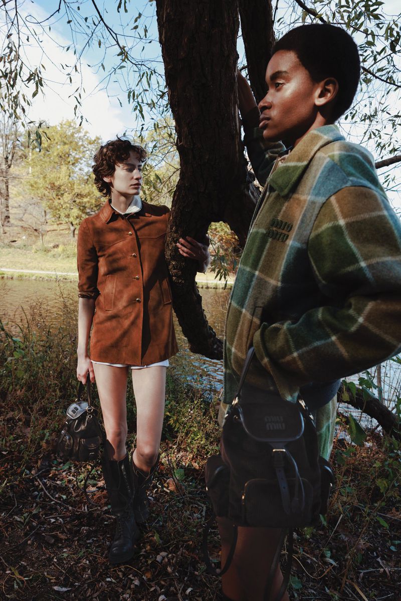 Glorianny Saint Fleur and Stella Hägerstrand pose near a tree outdoors wearing Miu Miu jackets and carrying bags.
