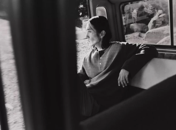 Black-and-white photo of a young adult leaning against a window inside a vehicle, gazing out at the outdoor landscape.