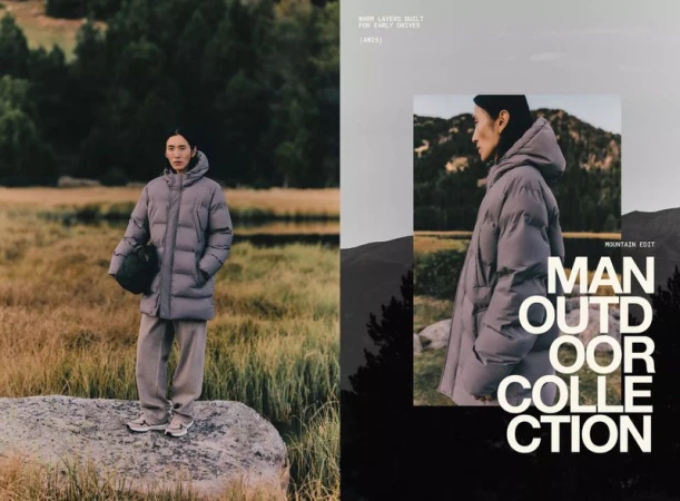 Fashion shot of a young adult male in a grey puffer coat and matching trousers standing on a rock in a field. 