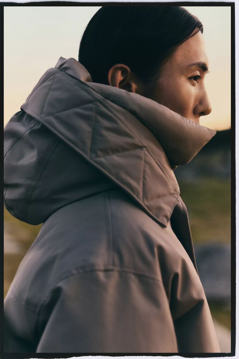 Profile portrait of an adult woman wearing a large gray quilted hooded coat outdoors in natural lighting.