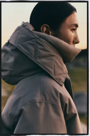 Profile portrait of an adult woman wearing a large gray quilted hooded coat outdoors in natural lighting.