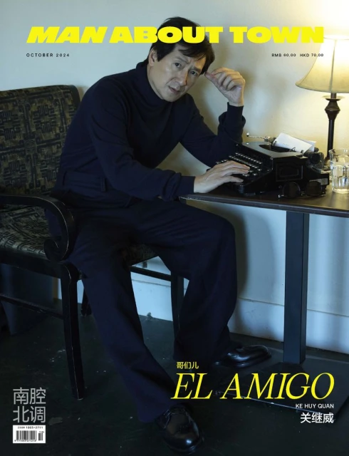 Magazine cover featuring Ke Huy Quan, seated at a table with a typewriter, styled in a navy turtleneck and slacks against a neutral backdrop.