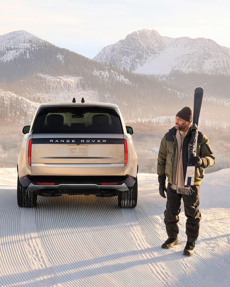 Range Rover SUV in a snowy mountain landscape with an adult male carrying skis. Vehicle and winter sports scenic view.