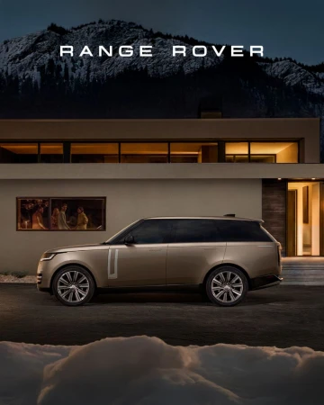 Champagne-colored Range Rover parked outside a modern house at night, with dark mountains visible in the background, emphasizing luxury and design.