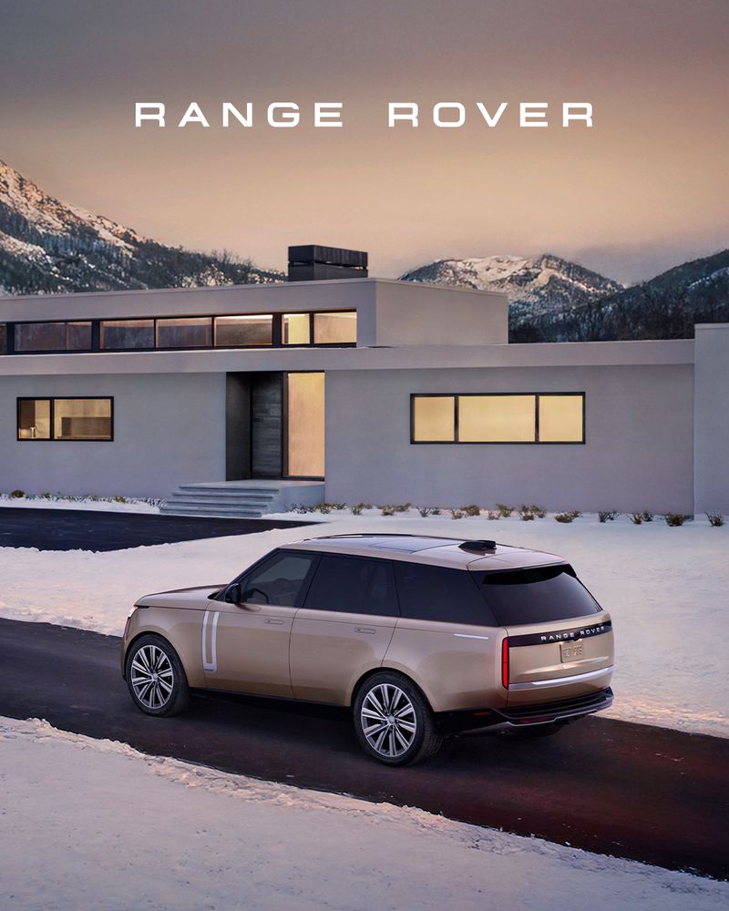 Beige Range Rover SUV parked on a snowy driveway in front of a modern house with snow-capped mountains in the background during dusk.