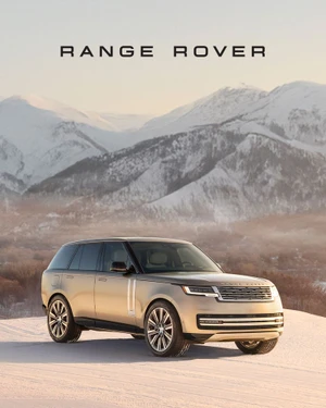 Gold metallic Range Rover SUV parked on a snow-covered hill with rugged snowy mountains in the background.