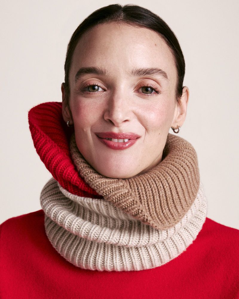 Close-up of a woman wearing a tan and red knitted cowl neck warmer and a red sweater, set against a neutral background.