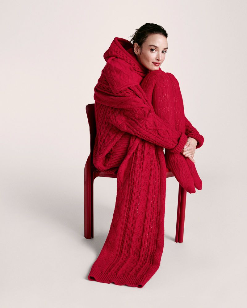 Woman in a vibrant red knit outfit posing on a chair against a neutral backdrop, fashion-forward portrait showcasing texture and color.