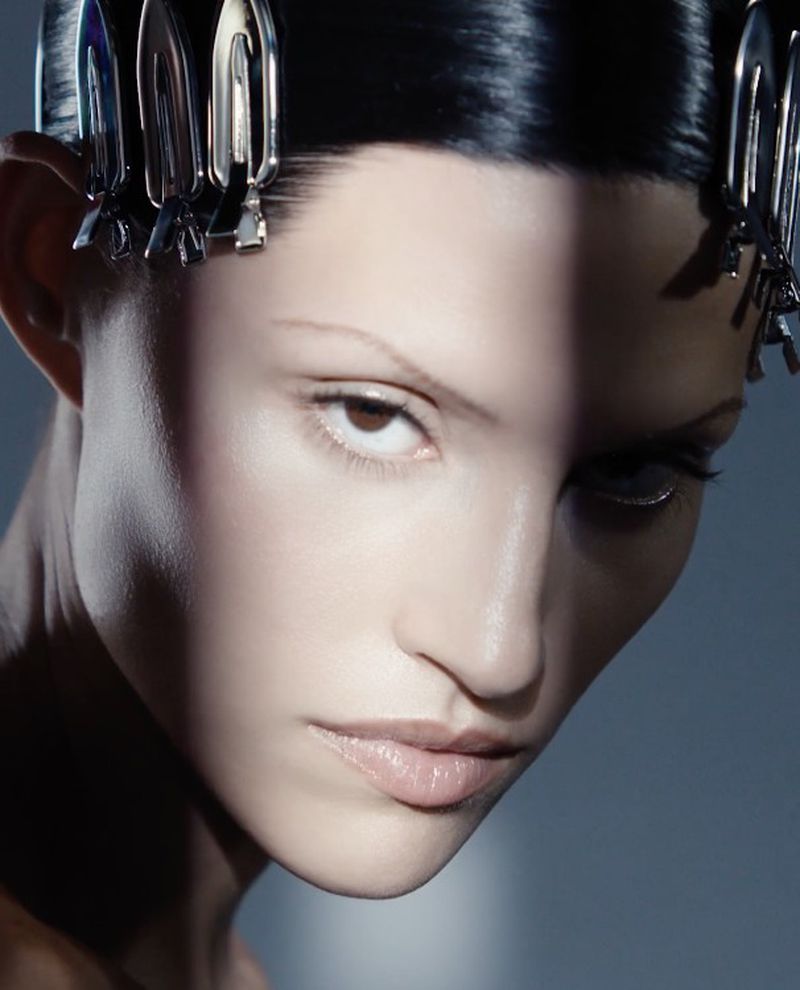 Close-up beauty shot of an adult female with slicked-back dark hair adorned with metal hair clips. High-key lighting and cool color palette.