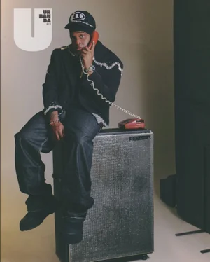 Man sitting on a speaker cabinet holding a red corded telephone receiver for Urbanda Magazine editorial by Angel Buzo