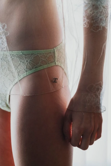Close-up shot of an adult female in pale green lace lingerie and a sheer patterned top, showcasing a fashion-forward aesthetic.