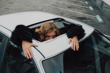 Model looking through a car sunroof wearing a black furry jacket for Unemployed Magazine Late Checkout project
