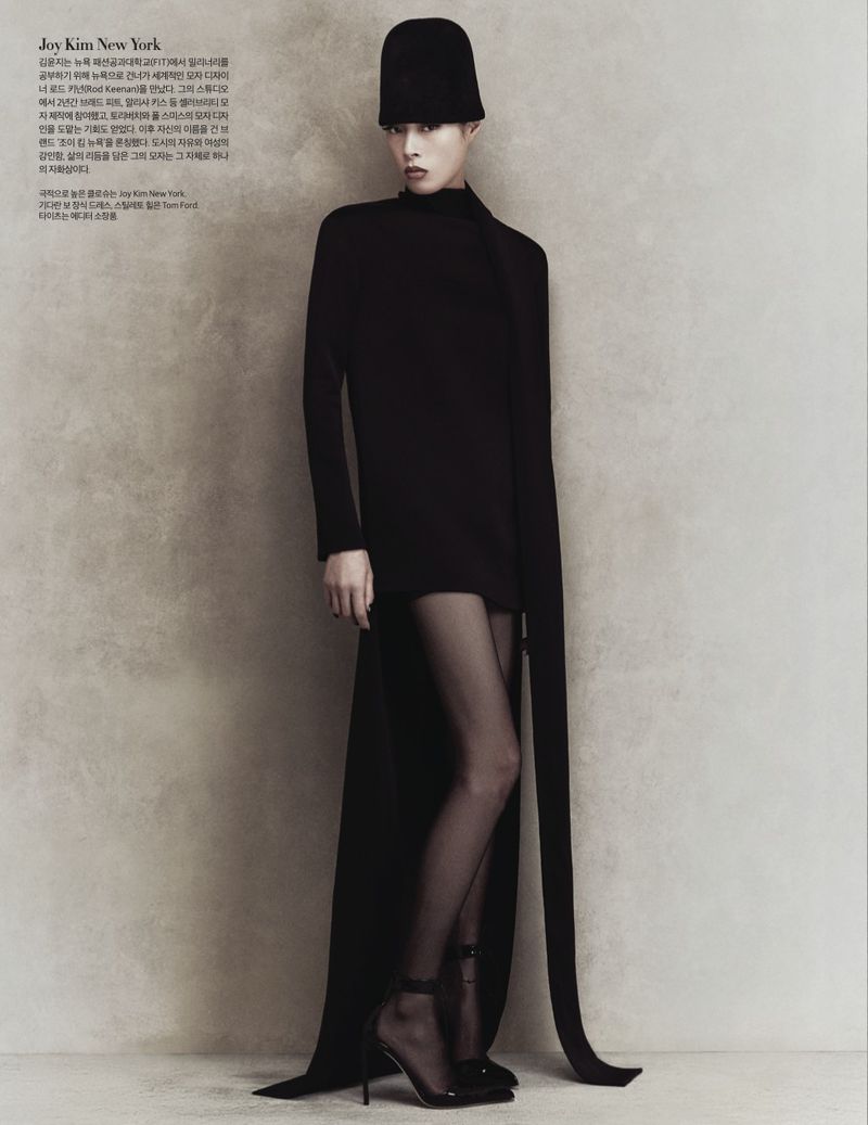 Fashion editorial shot of a slim adult woman in a black dress with long train and matching hat in a full-length studio shot.