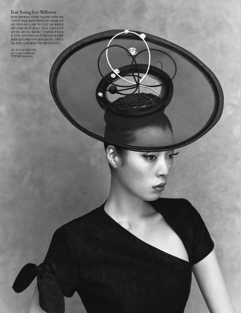 Black and white portrait of a stylish adult female wearing an elaborate hat with circular accents and a unique asymmetric dress.