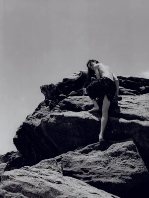 Model climbing dark rock formation against an overcast sky for Harper's Bazaar Brazil