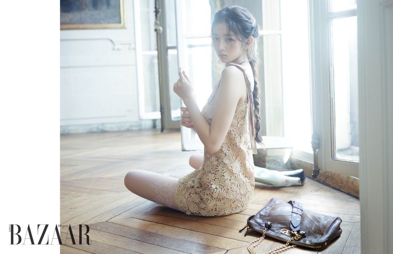 Indoor portrait of a young Asian woman in a lacy dress sitting on a wooden floor by a window with a leather bag nearby.
