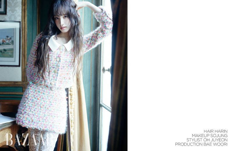 Indoor fashion shot of an Asian female model posing in a pink tweed suit with a white collared shirt, long hair, and bangs.