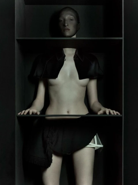 Artistic fashion studio portrait of a woman in a black outfit posing in a dark black box, showcasing unique style and design.