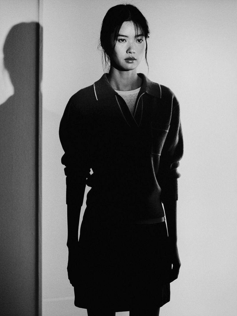Model Qianxia Ye wearing a dark collared shirt against a white wall with a harsh shadow cast in a black and white portrait.
