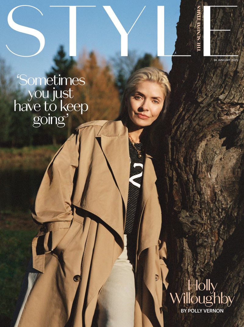 Holly Willoughby on a magazine cover wearing a tan trench coat next to a tree. The background includes a blue sky and green and brown trees.