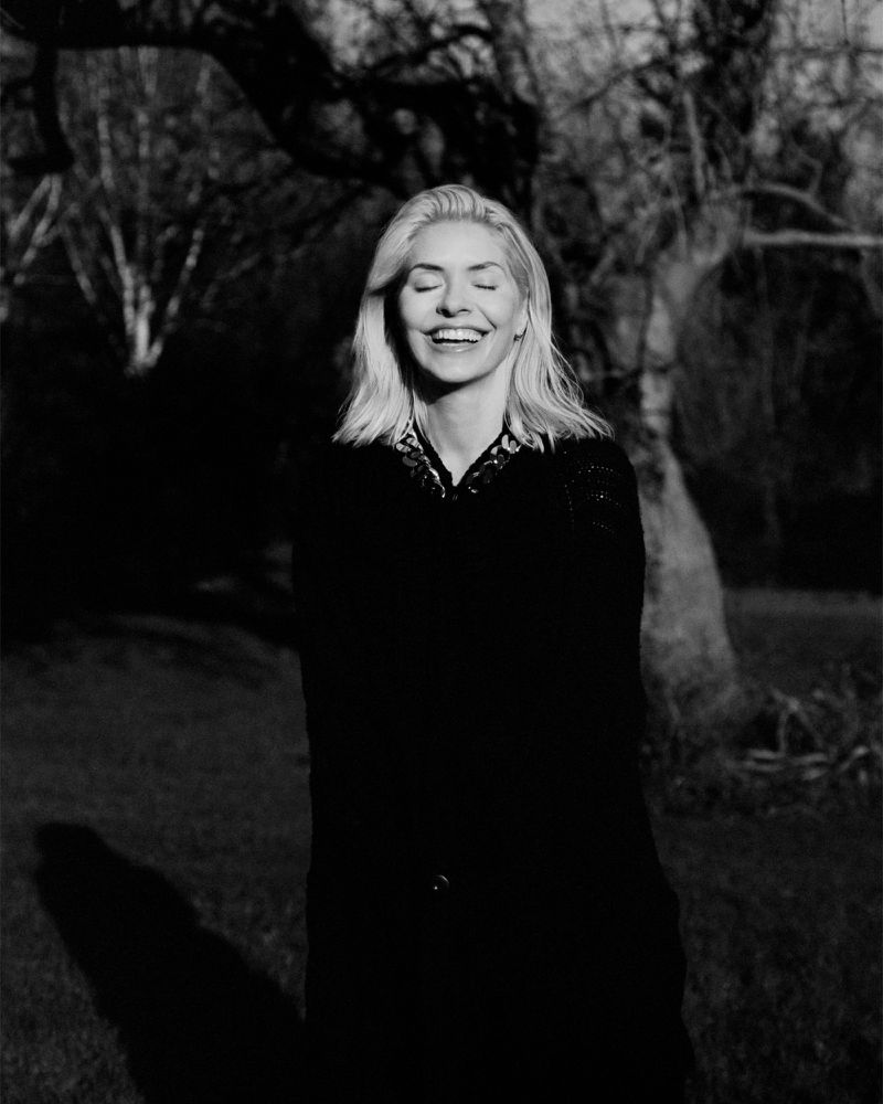 Black and white portrait of a smiling woman with blonde hair outdoors with trees in the background for The Sunday Times Style Magazine