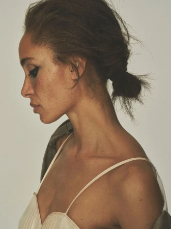 Model Adwoa Aboah in profile view wearing a cream slip top and dark jacket against a plain background for British Vogue