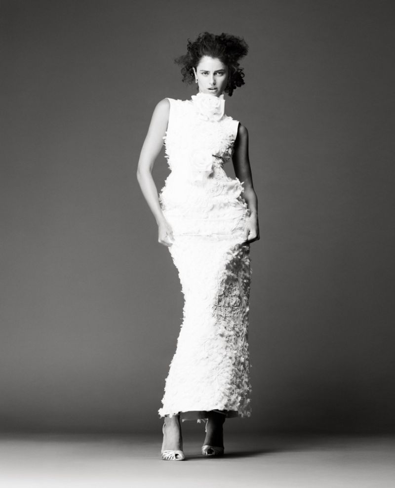 Elegant full-length portrait of a woman in a white, textured, formal dress and heels, posing in a photo studio against a grey backdrop.