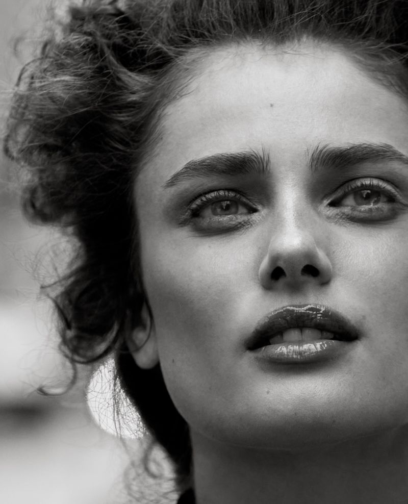 Monochrome portrait of an adult woman with curly hair looking up in a close-up shot with a shallow depth of field.