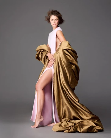 Model wearing pale pink dress draped in heavy gold metallic coat against a neutral grey studio background
