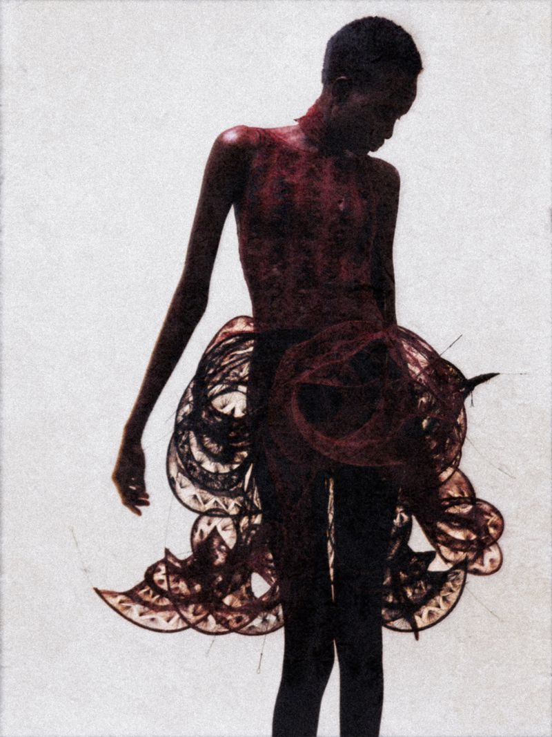 Artistic image featuring a slender, dark-skinned individual wearing a decorative skirt against a plain backdrop, with dominant red tones.