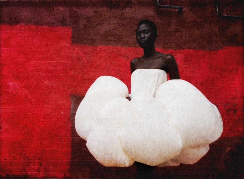 Woman in white strapless gown against red wall. Dark skin, formal dress. Elegant, high fashion portrait in urban environment.