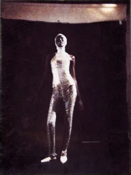 Model Aluel Keror in a white textured outfit and head covering standing against a dark backdrop for Rain Magazine La Voile.