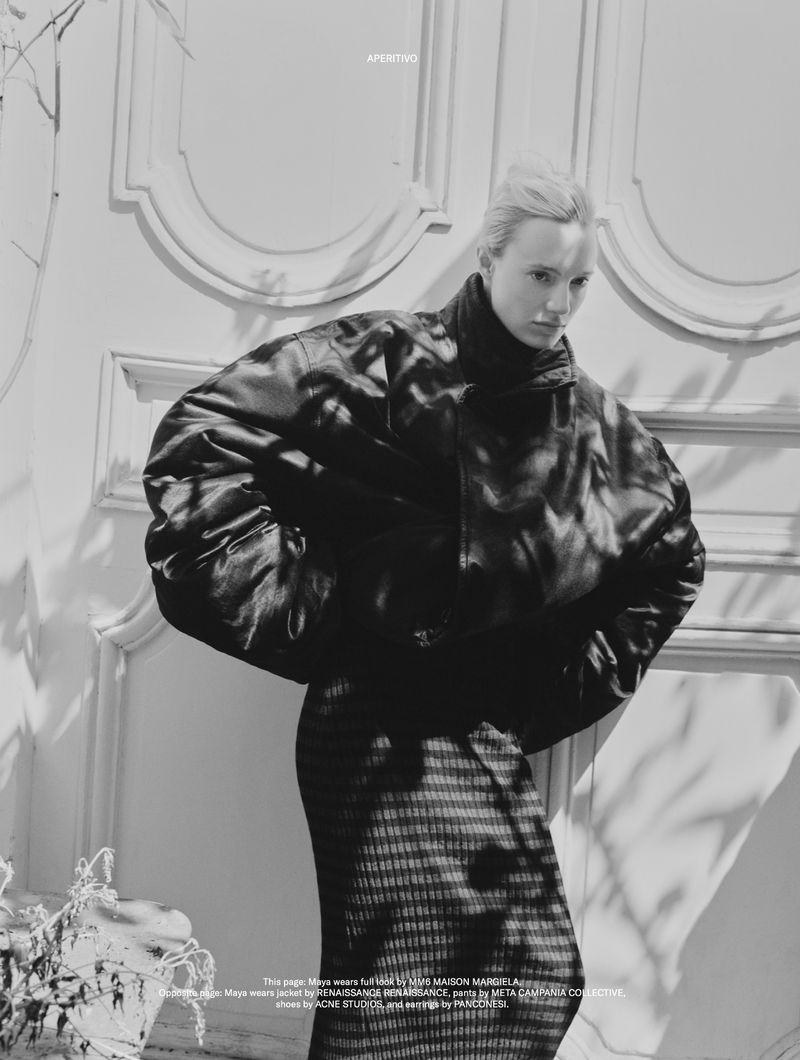 Black and white fashion portrait of model Maya Stepper wearing an oversized black bomber jacket and patterned skirt in dappled sunlight.