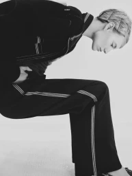 Model Maya Stepper wearing a dark track jacket and pants with striped piping against a plain white studio backdrop.