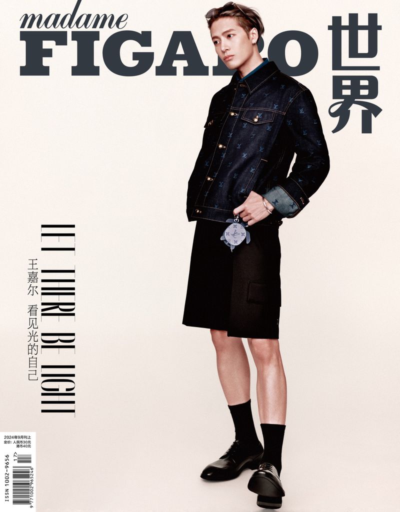 Jackson Wang posing in a dark denim jacket and shorts against a neutral studio background for a magazine cover.