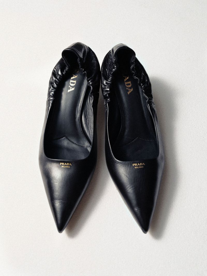 Two black leather Prada pointed-toe pumps displayed on a white surface, showcasing fashion footwear with visible logo detail.