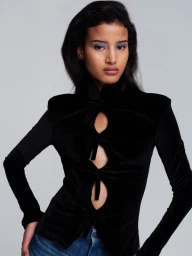 Model Khadija Lahmine wearing a black velvet cutout top and blue denim jeans against a plain grey seamless background.