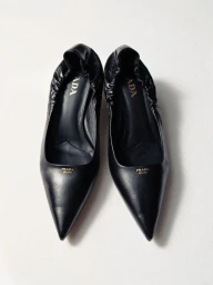 Pair of black pointed-toe Prada leather ballet flats with elasticated ruched collars on a seamless white surface.